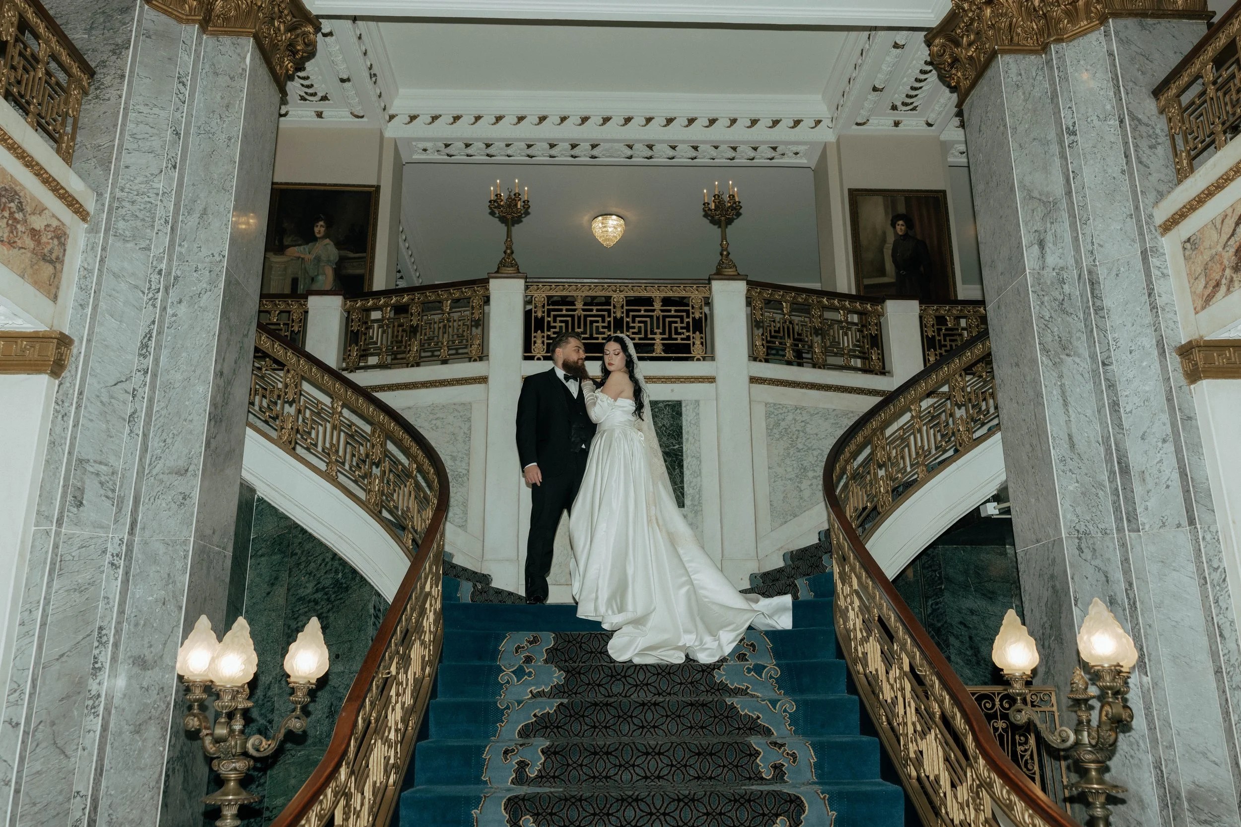 The bride and groom stand on the grand staircase of The Seelbach Hotel. A timeless, and cinematic moment surrounded by ornate gold detailing and historic elegance.